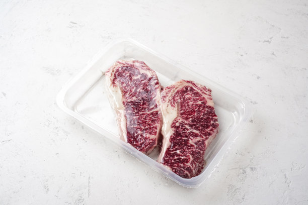 大理石般的神户牛肉生牛排，真空塑料包装，深色石头背景图片下载