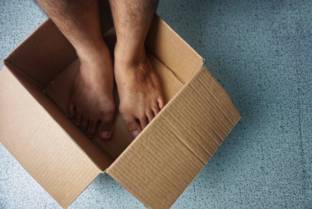 东南亚男子光着脚站在纸板箱里，高角度观看图片下载