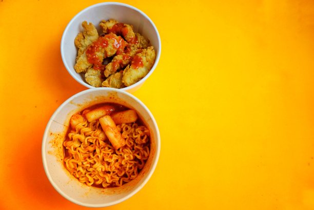 韩国街头小吃，麻辣的toppoki面条和油炸鸡肉馄饨，纸碗，橙色背景图片下载