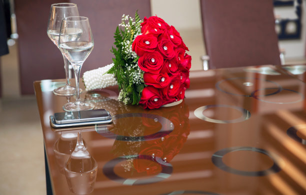 一束红色的婚礼花。婚礼上的红玫瑰花束和两个香槟杯站在正品上。背景与眼镜和鲜花。图片下载