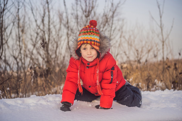 男孩穿着红色的时装在户外玩耍。与孩子们在寒冷的冬天进行积极的休闲活动。男孩玩第一场雪。快乐的小朋友在雪地里玩耍，好天气图片下载