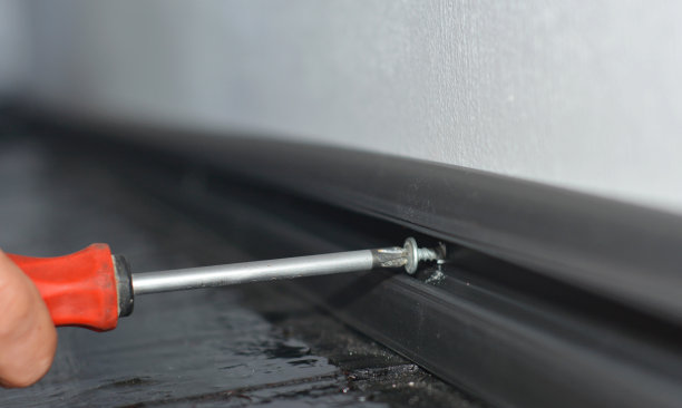 一个工人正在安装一个黑色的塑料踢脚板，地板底座和一个空间隐藏电缆使用螺丝和螺丝刀。图片下载