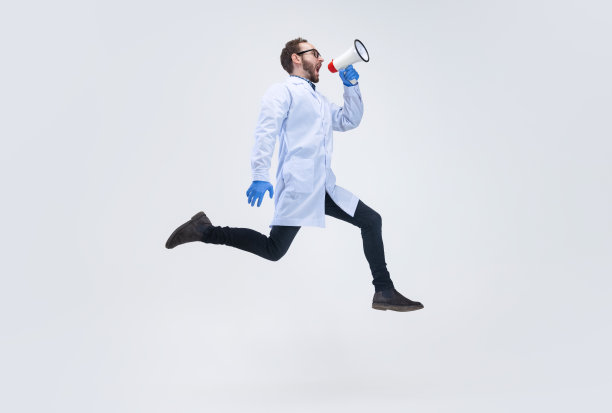 一个兴奋的男人，药剂师，医生对着隔离在白色背景下的扩音器跳着大喊着。图片下载