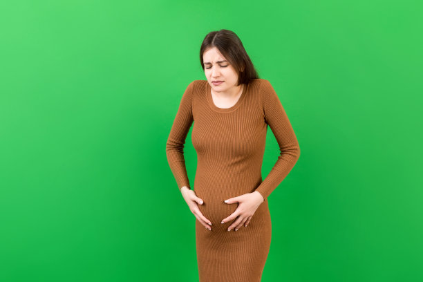 一个肚子痛的怀孕女孩站在彩色背景上。孤立的图片下载
