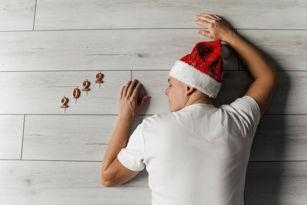 一个年轻人戴着圣诞老人的帽子躺在地板上。2022号图片下载