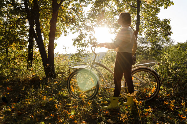 一个年轻的短发女子，穿着白色的毛衣，骑着自行车，站在秋日的森林里。图片下载