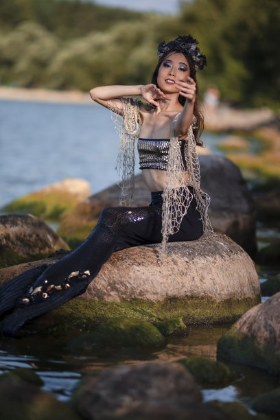 渴望美人鱼在网在岩石海岸穿着贝壳装饰的皇冠和黑色闪亮的尾巴在性感的身体上覆盖着Strasses作为海的情妇女王。垂直的形象定位图片下载