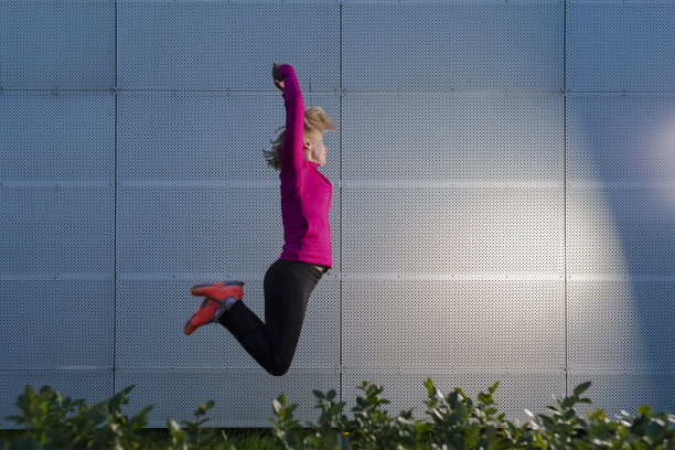 在抽象金属墙背景下进行户外跳跃训练的成熟女运动员。水平图像组成图片下载