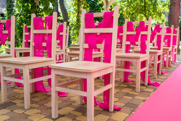 拱门两边都有粉红色的婚礼椅。粉红色装饰的婚礼场地，户外为客人准备的木椅。粉红色的婚礼图片下载