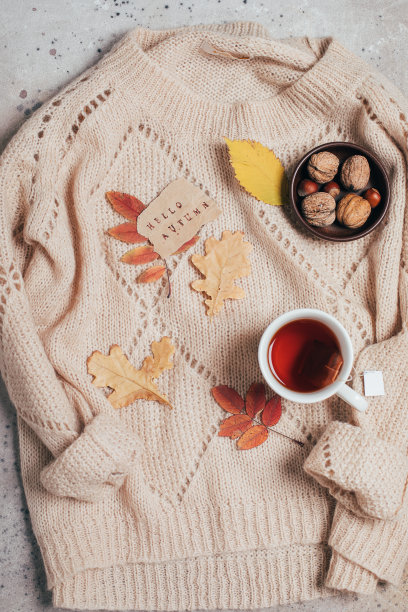 平躺着一杯茶，注着文字问候秋色缤纷的秋叶，毛衣上挂着坚果。图片下载
