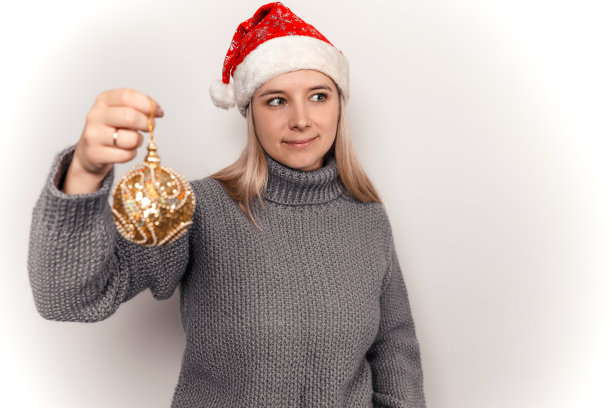 一个身穿灰色羊毛衫、头戴圣诞帽的女人手里拿着圣诞装饰品图片下载