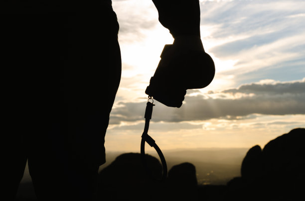 近景剪影自由年轻男子摄影师背包客徒步旅行和手持相机站在山顶图片下载