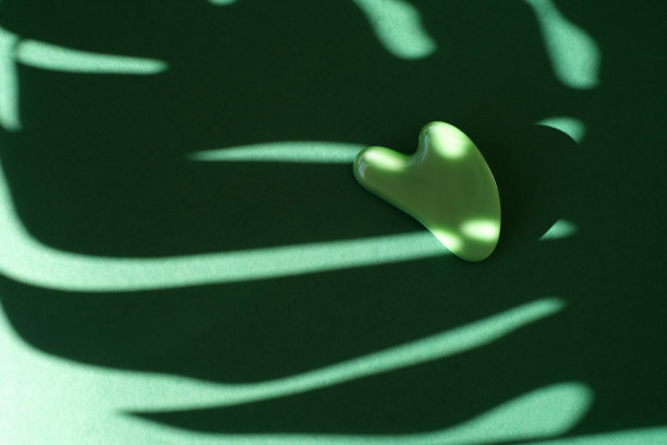 在家使用刮刀进行面部按摩，背景为绿色纹理图片下载