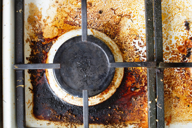 煤气炉表面脏。大型煤气炉和煤气炉的铸铁炉排，周围环绕着剩饭剩菜和饮料。顶部区域表面和燃烧器头需要清洗烧焦的油脂图片下载