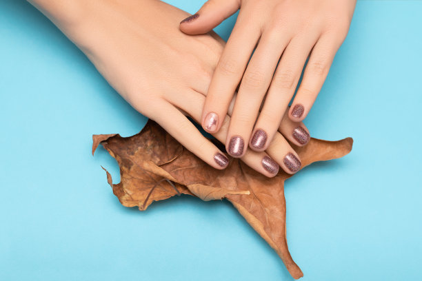 女性手与棕色指甲设计。闪亮的棕色指甲油指甲与明星指甲艺术。女人手里拿着干树叶。图片下载