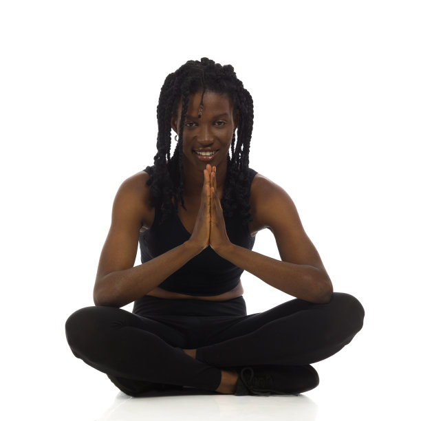 身着运动服的微笑的非洲裔美国妇女双手合十地坐在地板上。正面，全长。图片下载