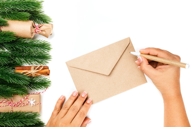 为工艺信封给圣诞老人的信的模型，妇女手写在信封上与工艺笔，孤立在白色背景与圣诞节设计图片下载