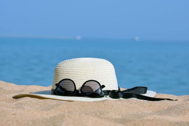 温暖的阳光下，热带海滨沙滩上黄色草帽和黑色防护太阳镜的特写。暑假的概念。图片下载