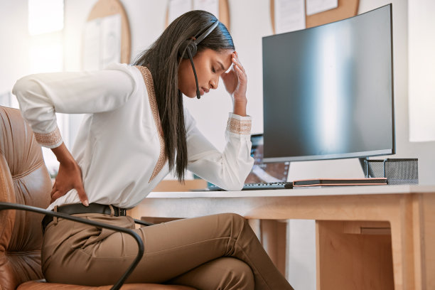 一名迷人的年轻女性呼叫中心工作人员在办公室用电脑工作时遭受背痛的折磨图片下载