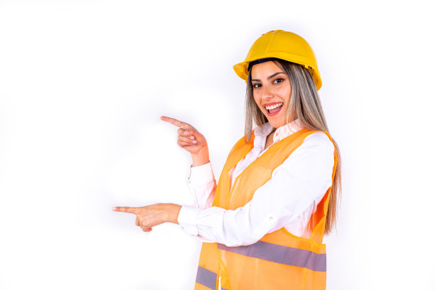 美丽的年轻女工程师或主管，穿着安全装备，指着白色背景上有文本或复制空间的一侧。赋权女性的概念，职业女性。图片下载