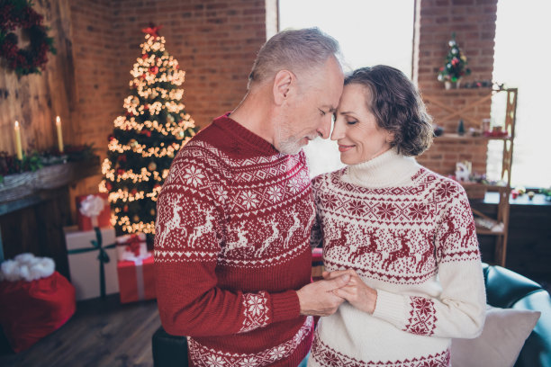 照片中的老夫妇手牵着手，穿着红色的节日毛衣，在装修好的房子里图片下载