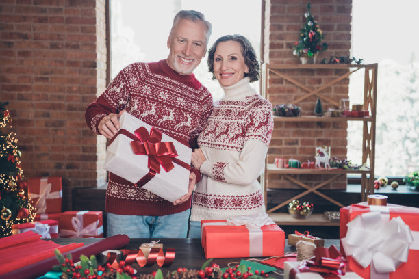 照片中，两个已婚的父母手里拿着礼物包，眉开眼笑，穿着装饰套头衫回家图片下载
