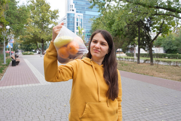 公园里一个黑发女人拿着一塑料袋水果。图片下载