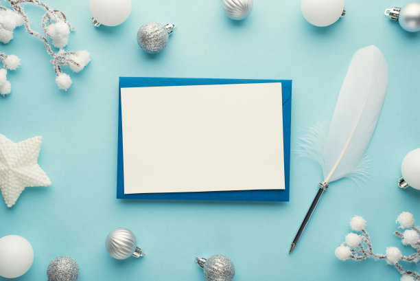 顶部视图照片卡在蓝色信封，羽毛笔，白色和银色圣诞树装饰，星星球和雪树枝在孤立的淡蓝色背景与空白图片下载