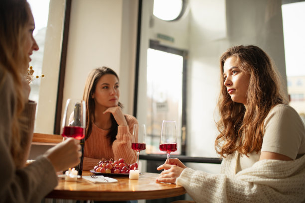 三个美丽的女人坐在咖啡馆里，一边聊天一边喝着红酒。周末聚会图片下载