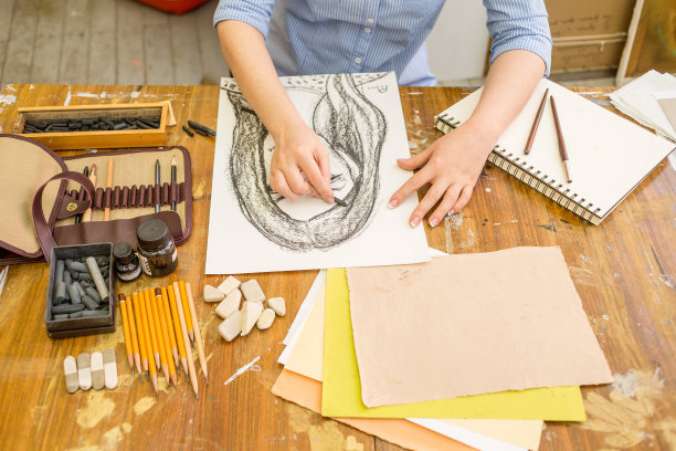 一个小女孩正在纸上画一幅天然木炭的素描。桌子上的艺术家有不同的绘画用品图片下载