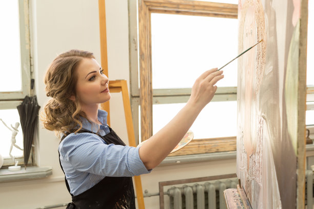 一位年轻的画家在画室里用油画画。桌子上的艺术家有不同的绘画用品图片下载