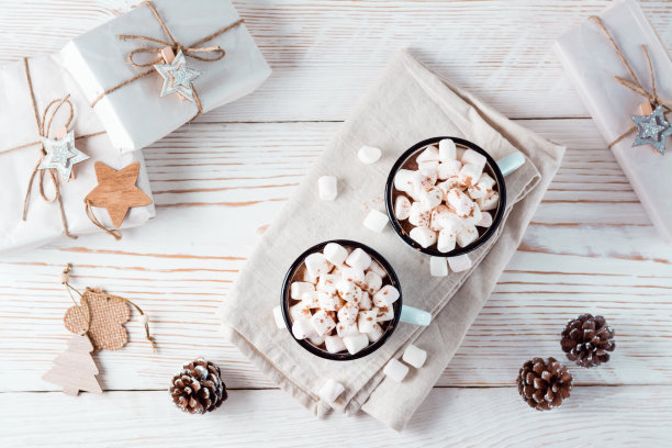 白色木桌上，圣诞装饰着两个装满可可和棉花糖的马克杯。环保节日。俯视图图片下载