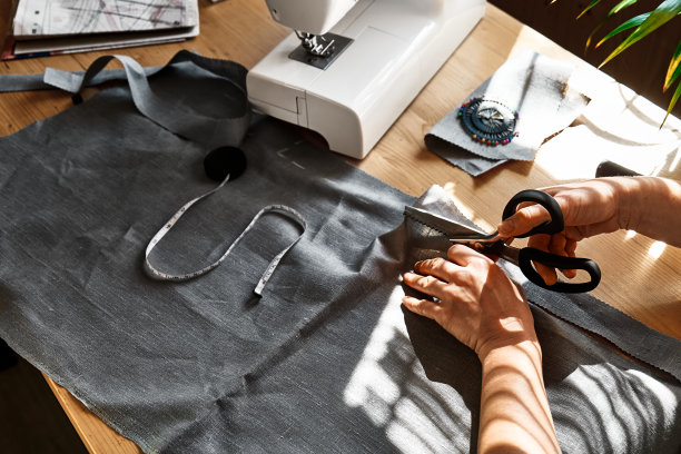 一位妇女正在用亚麻布裁剪一张图案纸。女裁缝在小工作室的缝纫机上缝纫。时尚工作室，剪裁，手工制作服装的概念。慢时尚意识消费图片下载