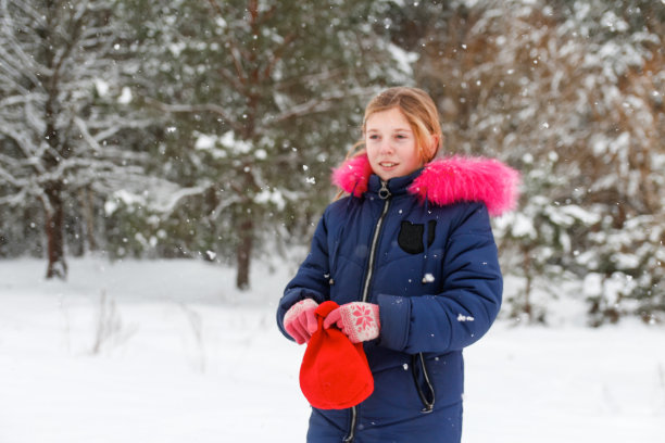 离焦的肖像，十几岁的快乐女孩脱下红色的温暖的帽子在自然冬天雪林背景。漂亮的孩子在室外微笑，寒冷的天气。白种人的孩子。十几岁的暴乱。的焦点图片下载