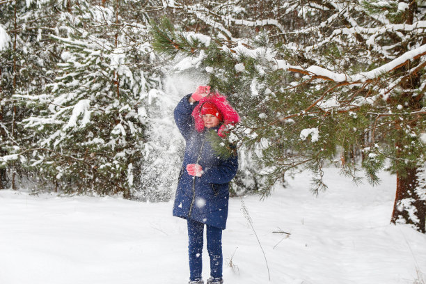 十几岁的快乐女孩在红色温暖的帽子摇雪从一个树枝外面的自然冬天雪森林的背景。漂亮的孩子在户外，寒冷的天气。白种人的孩子。节日快乐图片下载