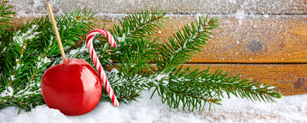 圣诞节的时候，红色的蜜饯苹果和带冷杉树枝的糖果拐杖和木制背景上的雪图片下载