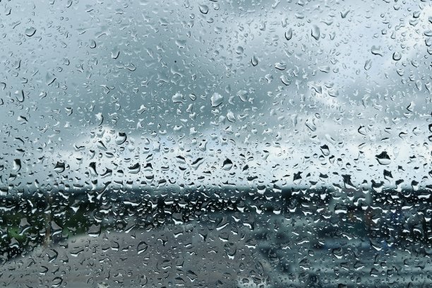 雨点落在透明的玻璃上。美丽的雨天空与城市背景。图片下载