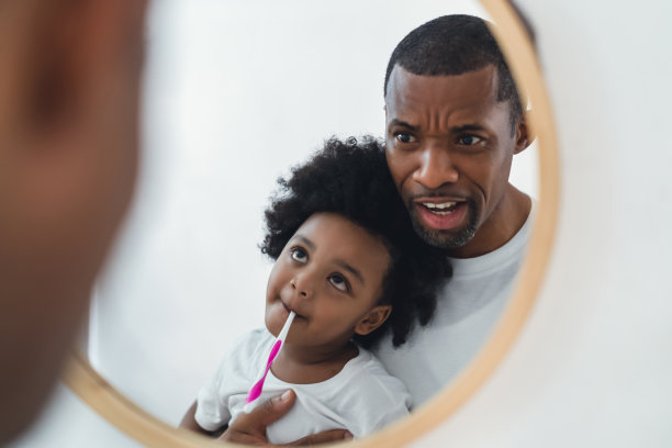 快乐的非裔美国人父亲和小儿子一起玩，一起刷牙，在家里的浴室里看镜子。口腔卫生，早上在浴室的惯例。图片下载
