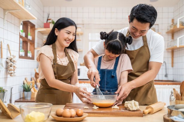 亚洲人幸福的家庭呆在家里的厨房，烘焙面包和食品。年幼的小女孩从父母那里学习做饭，父亲和母亲在家里享受亲子关系。图片下载