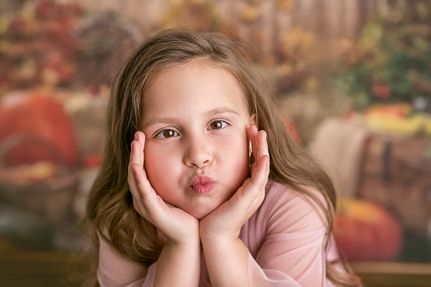 照片上的女孩穿着粉红色的裙子，沉迷在镜头前——鼓鼓的眼睛，露齿的微笑，撅起的嘴唇。有趣的脸。黑暗的背景。有选择性的重点。图片下载