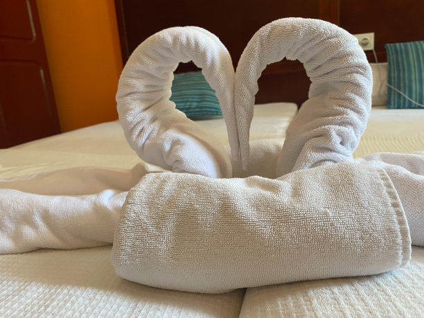 酒店房间的床上有两只毛巾天鹅、鲜花和装有香槟的冰桶图片下载