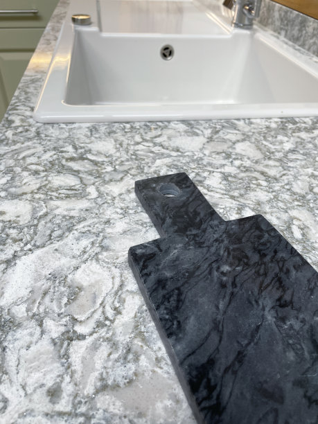 除了现代的长方形厨房水槽和排水板，白色陶瓷贝尔法斯特水槽，黑色大理石砧板在灰色和白色花纹花岗岩台面上的特写图像，聚焦前景图片下载