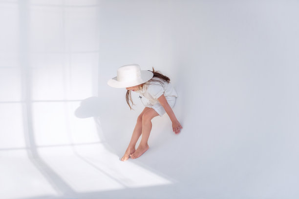 小女孩在地板上玩的很开心，戴着时髦的帽子，在一个白色的阁楼内部和通风的织物。图片下载