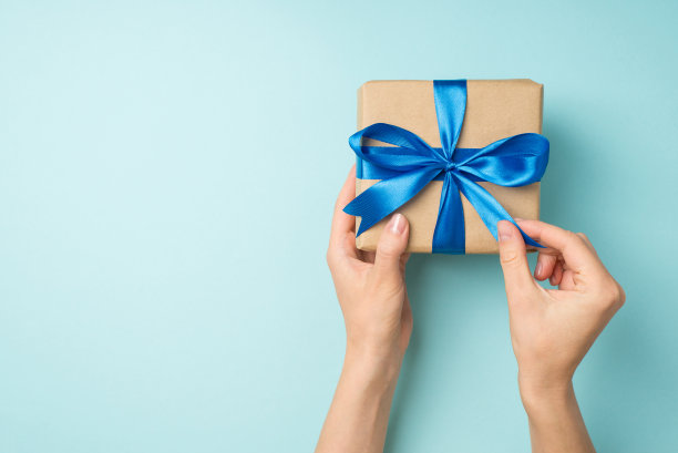 第一人顶视图照片的手打开工艺纸礼品盒与蓝色丝带蝴蝶结孤立的淡蓝色背景与copyspace图片下载