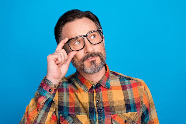 照片人像男子戴着眼镜，若有所思地望着空旷孤立的亮蓝色背景图片下载