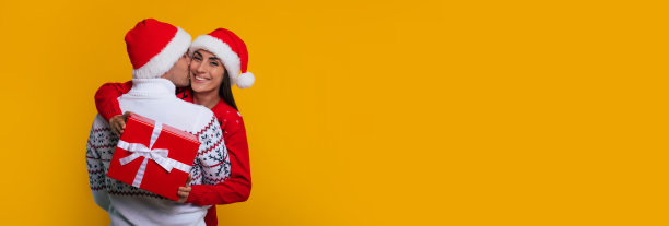 宽幅横幅照片，美丽快乐的年轻夫妇在圣诞节的圣诞老人的帽子，而他们庆祝新年和女人给她的男朋友惊喜图片下载