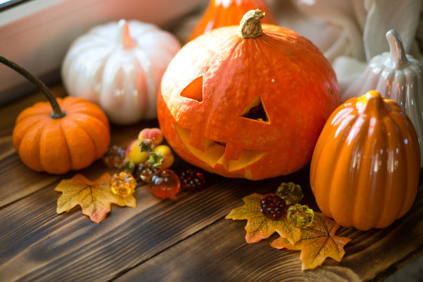 橙色和白色的南瓜和杰克灯笼，他的眼睛和嘴巴在木桌上与黄色的秋天枫叶，浆果。秋天心情，万圣节，家居装饰图片下载