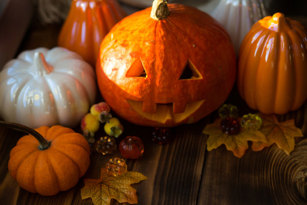 橙色和白色的南瓜和杰克灯笼，他的眼睛和嘴巴在木桌上与黄色的秋天枫叶，浆果。秋天心情，万圣节，家居装饰图片下载
