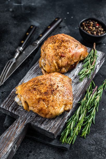 香辣烤鸡腿在木板上与迷迭香。黑色背景。俯视图图片下载