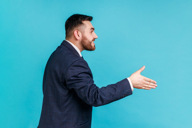 你好，很高兴认识你！友好的微笑英俊男人穿着正式的西装伸手，在面试中提供握手，侧面图。图片下载